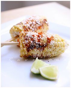 two grilled corn on the cob with sugar and limes next to it