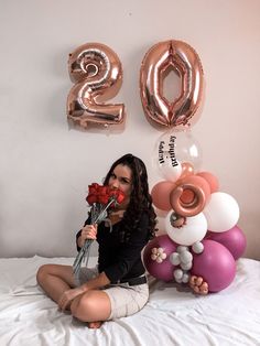 a woman sitting on a bed with balloons and flowers in front of the number 20 sign