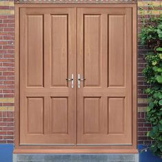 two wooden doors are shown in front of a brick wall and green plants on either side