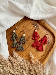 three tasseled earrings sitting on top of a wooden tray next to dried grass