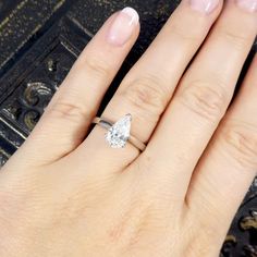 a woman's hand with a diamond ring on top of her finger and the other hand holding an engagement ring