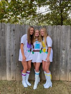 three girls dressed up in costume standing next to a wooden fence and wearing white boots