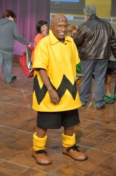 a man in a yellow shirt and black shorts standing on a wooden floor with other people