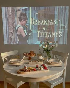 there is a table with food on it and a large screen behind it that says breakfast at tiffany's