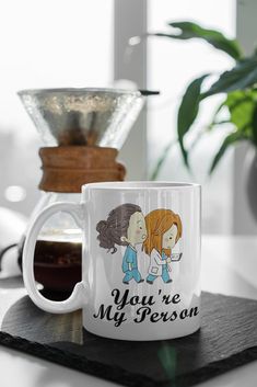 a coffee mug with the words you're my person on it next to a potted plant