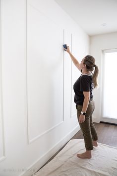 a woman is painting the wall with white paint