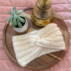 a crocheted headband sits on a wooden plate next to a potted plant