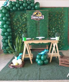 there is a table with balloons and other decorations on the floor in front of a green backdrop