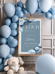 a baby shower sign with balloons and a teddy bear sitting in front of the frame