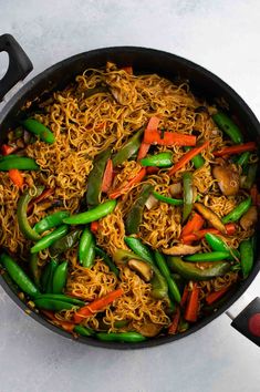 a wok filled with noodles and vegetables on top of a white counter next to utensils