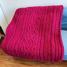 a pink knitted blanket sitting on top of a wooden floor next to a blue couch