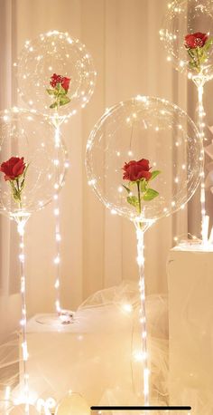 two clear balloons with roses in them on a white table cloth and some lights around it