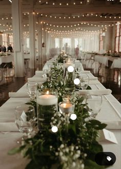 a long table with candles and greenery on it in a room filled with tables