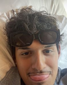 a man laying in bed with sunglasses on his head