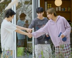 two boys are shaking hands in front of a store window with another boy standing next to them