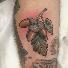 a close up of a person's leg with a tattoo on it that has leaves and acorns