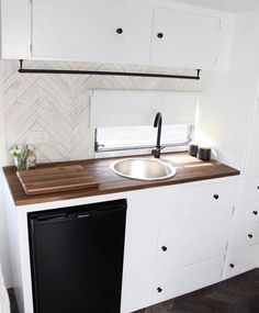 a kitchen with white cabinets and wood counter tops, black dishwasher and sink