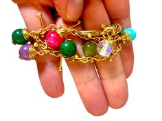 This handcrafted colorful orb link bracelet has a unique design that alternates with two sizes of dyed agate with the larger stones semi-enclosed in a woven pattern. This organic-style bracelet will bring an eye-catching flair to any outfit. Add some bold color to your jewelry collection with this stunning, unique accessory. Its a wonderful piece to mix and match with your favorite bracelets to create a personalized look. These bracelets can easily go with many of our necklaces, specifically these chain necklaces with colorful suspended gemstones as the design is most similar. Details: Colorful orb link bracelet with beads and added along the length of the bracelet. The bracelet has a lobster clasp closure. Size: Length of bracelet ~ 6" (15 cm) - with an additional 1" of chain to customize Elegant Multicolor Cabochon Bracelets, Multicolor Cabochon Bracelet, Multi Colored Jade Bracelet, Unique Multicolor Multi-stone Bracelet, Formal Multicolor Multi-stone Bracelets, Bracelet With Beads, Dyed Agate, Green Chalcedony, Woven Pattern