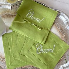 green napkins with white writing on them sitting on a silver tray next to flowers