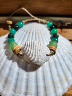 a sea shell and green beaded bracelet sitting on top of a seashell