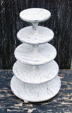 three tiered white cake stand on top of a wooden table next to a black wall