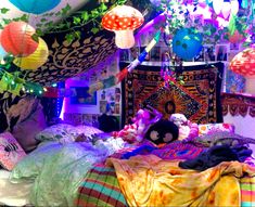 a bed covered in lots of pillows and blankets under colorful lights hanging from the ceiling