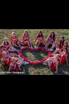 a group of women in red and white outfits sitting on the ground with a heart shaped wreath