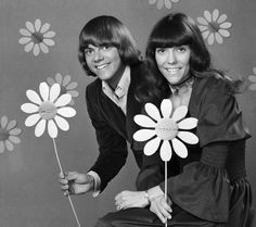 two women sitting next to each other with flowers in front of their faces, one holding a pinwheel