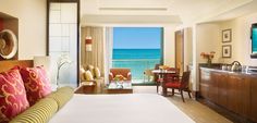 a hotel room with a bed, desk and television in front of an ocean view