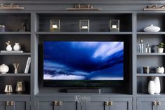 a flat screen tv sitting on top of a wooden shelf in front of a gray bookcase