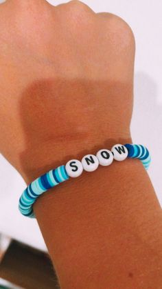 a person wearing a bracelet with the word snow written in white and blue beads on it