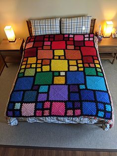 a bed covered in a multicolored blanket next to two lamps