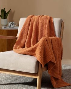 a chair with a blanket on top of it in front of a table and potted plant