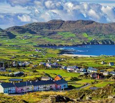 a small town on the coast with mountains in the background and blue water behind it