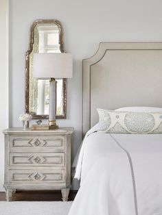 a white bed sitting next to a dresser with a mirror on it's side