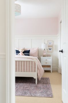 a pink and white bedroom with a teddy bear sitting on the end of the bed