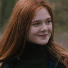 a close up of a person with long red hair wearing a black jacket and smiling