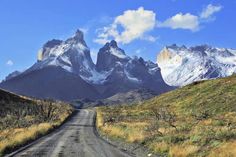 a dirt road in front of mountains with snow on the tops and grass growing all around