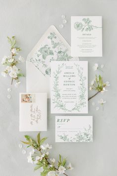 the wedding stationery is laid out on top of each other, with white flowers and greenery