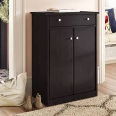 a black cabinet sitting in the corner of a room next to a rug and pillows