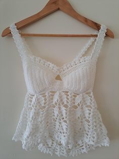 a white crochet top hanging on a wooden hanger