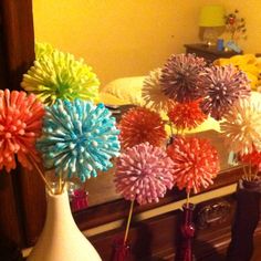 colorful paper flowers are in vases on the floor next to a fireplace mantel