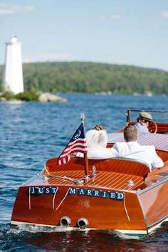 two people in a wooden boat with an american flag on the front, and a lighthouse in the background