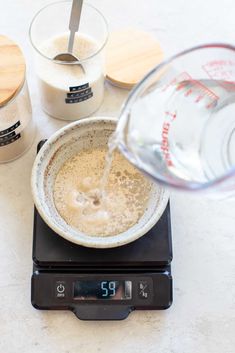 a person pouring water into a bowl on top of a scale with measuring cups next to it