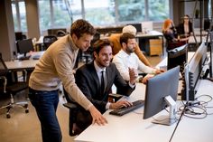 three men in an office setting looking at a computer screen and smiling while another man looks on