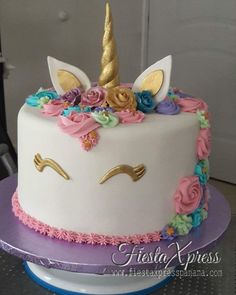 a white cake decorated with flowers and a gold unicorn horn on top is sitting on a purple plate