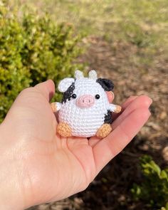 a hand holding a tiny crocheted cow in it's left hand, with shrubbery in the background