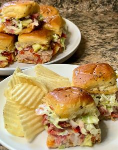 two plates filled with sandwiches and chips on a counter top next to another plate full of potato chips