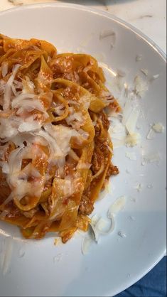 a white plate topped with pasta covered in sauce and cheese on top of a blue table cloth