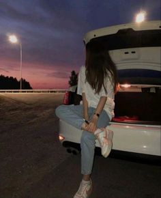 a woman sitting on the back of a white truck at night with her legs crossed